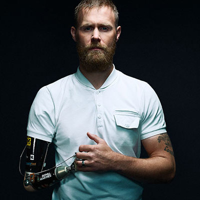 Portrait of guest speaker, Invictus Games gold medallist, Mark Ormrod, showing his prosthetic arm and stood strongly.