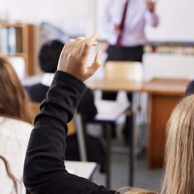 School students at desks with one child raising their hand.